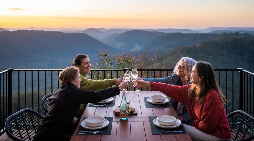 Four people clinking glasses over a dinner table with beautiful mountains and the sunset in the background.