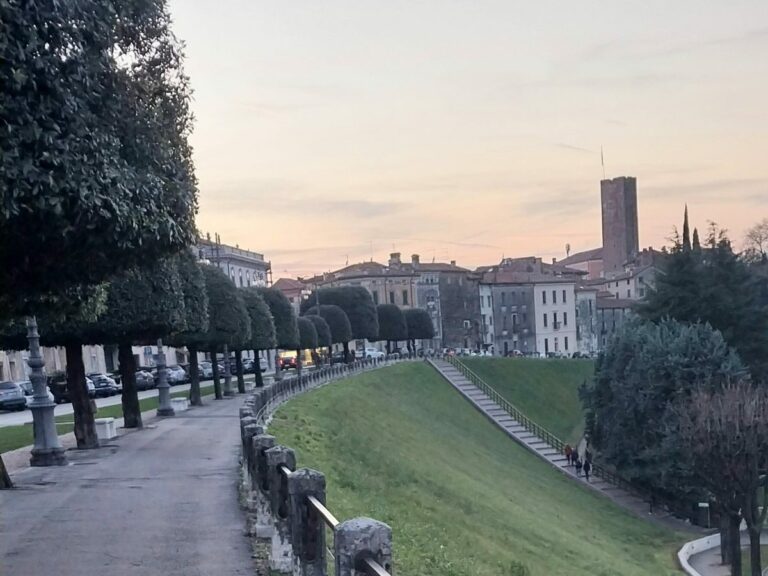 Tree-lined walking path along Viale dei Martiri in Bassano del Grappa at dusk, overlooking European architecture