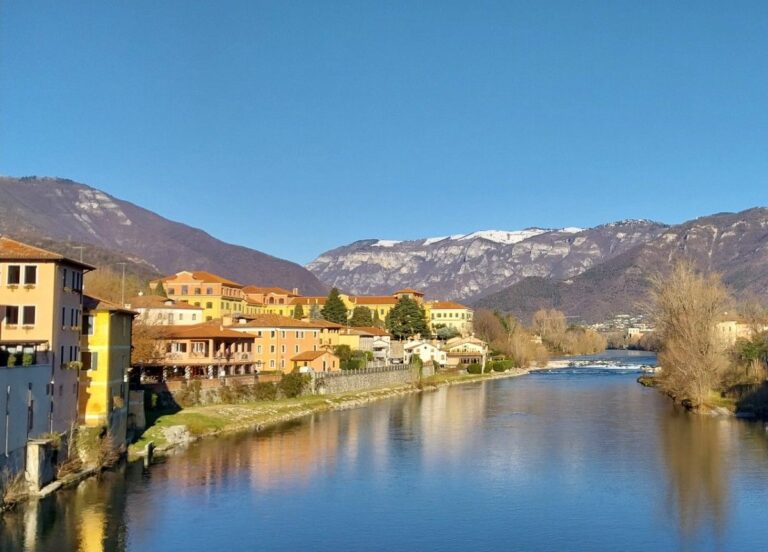 Historic Italian riverside town with colourful buildings and mountains reflected in calm river water