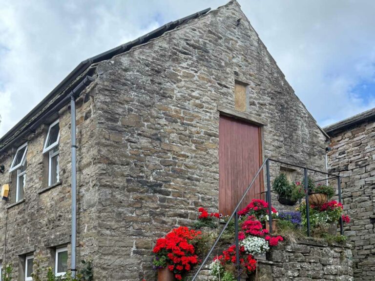 Historic stone cottage with red door and flowering plants in Yorkshire