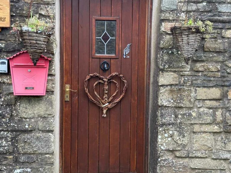Traditional stone cottage doorway with woven heart wreath and pink letterbox