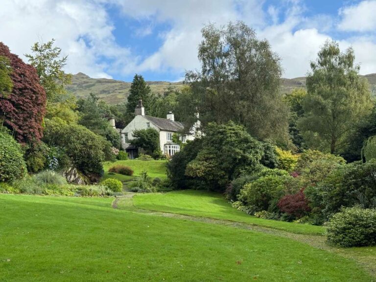 Stone cottage nestled in lush valley gardens with rolling hills and mature trees
