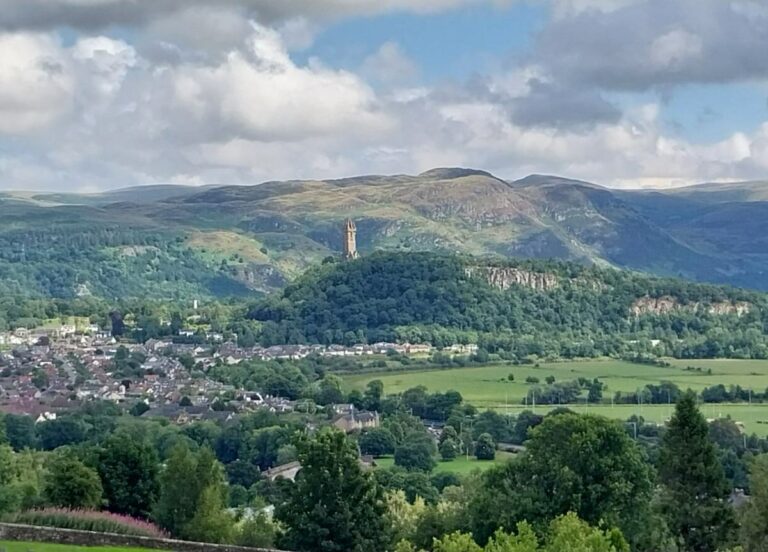 Scenic view over the countryside and we can see a town and historical monument standing on a hill in the distance.