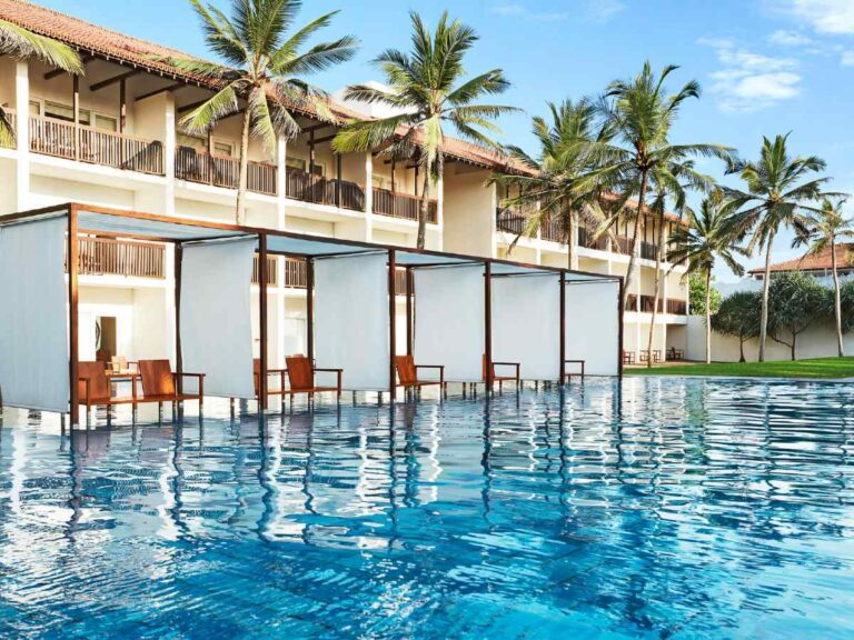 Resort poolside view showing blue water and apartments in background.