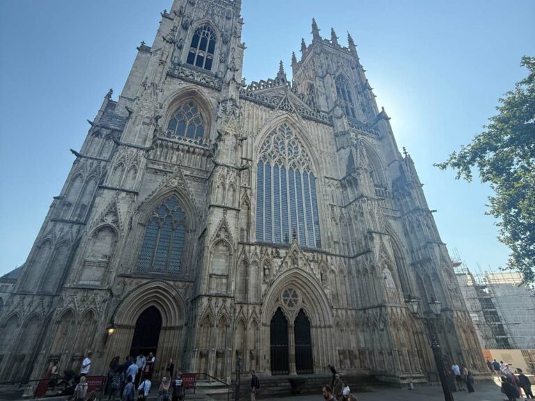 Impressive Gothic Cathedral towers above blocking the sun, people walk up it's stairs to enter this magnificent church.
