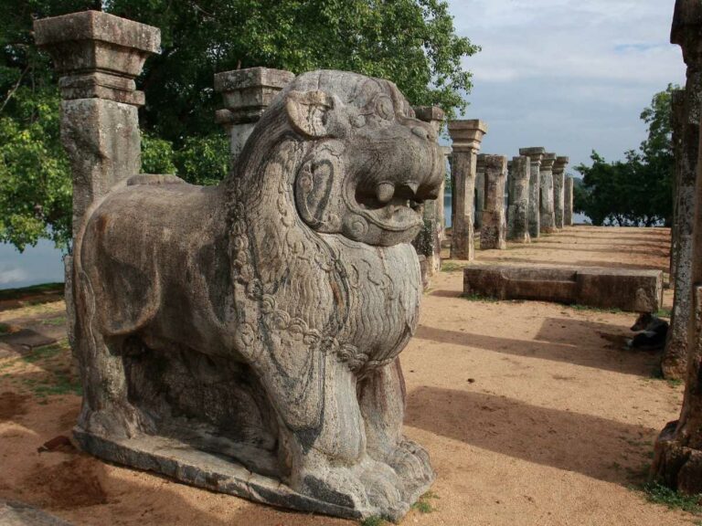 Lion statue with other statues lined up behind it at historical ruins site.