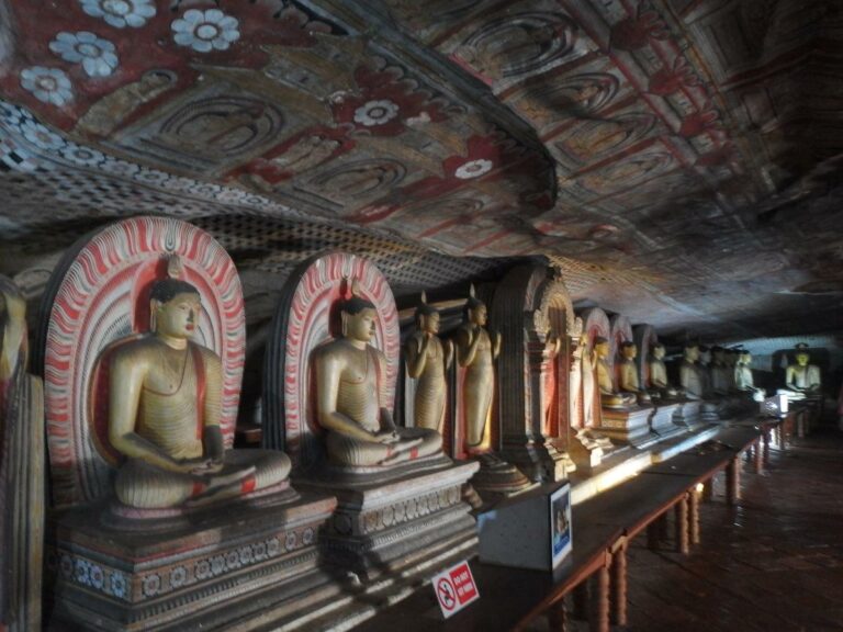 Cave temple showing golden statues of Buddha and paitings covering the cave walls.