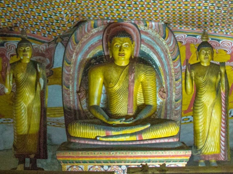 Statue of golden Buddha alongside other statues in a cave temple.