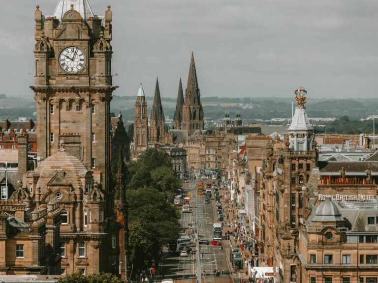 Looking down the busy main road where there is are medieval buildings, spires and a clock tower.