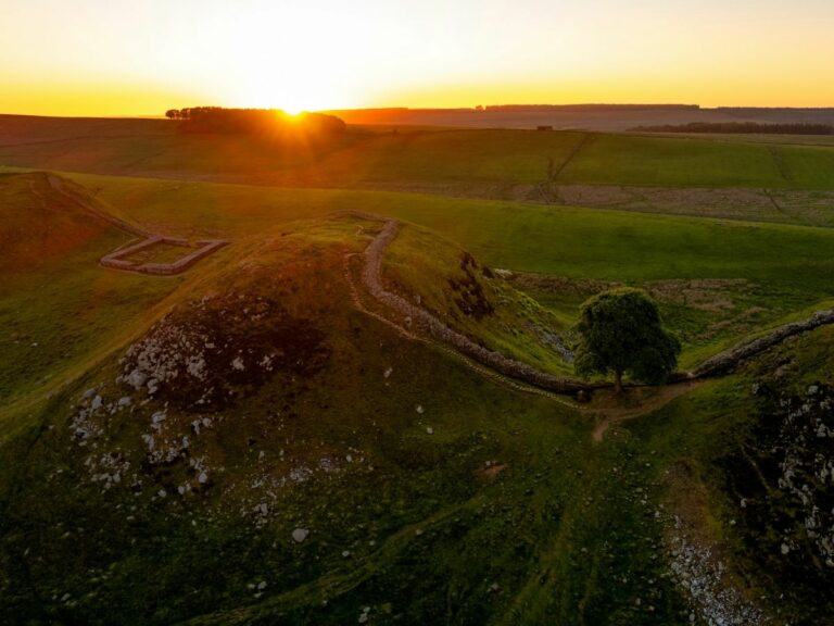 The sun sets over the hills showing the stone wall across the landscape.