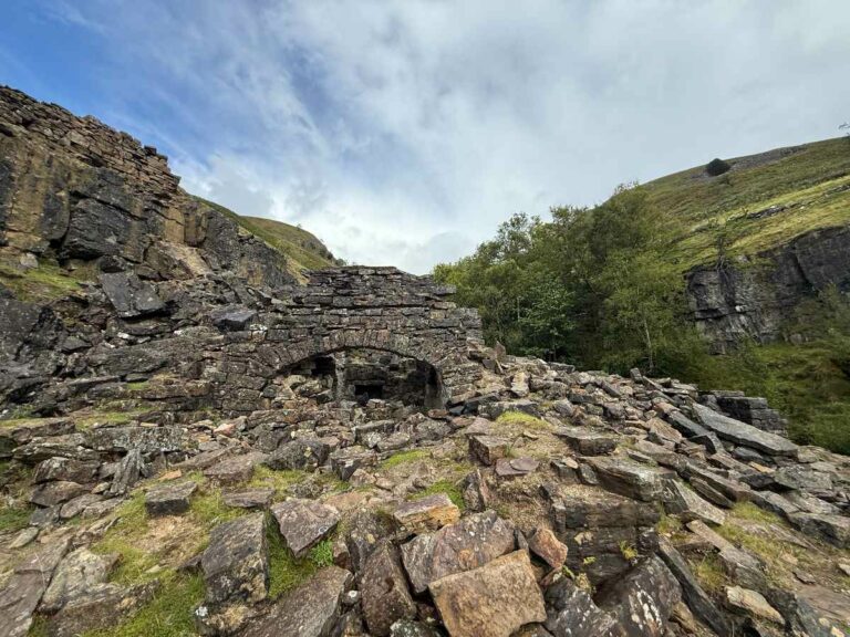 Historic stone bridge ruins nestled in moorland valley with walking trails through natural landscape