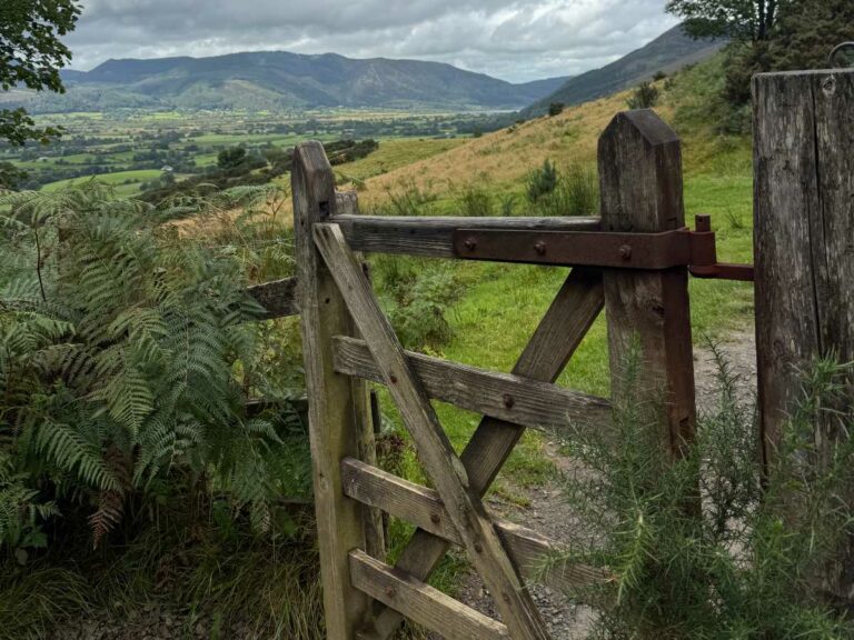 Wooden gate opening onto hillside meadow with valley and mountains visible beyond