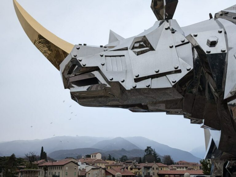 Giant metal rhino sculpture looms over historic Italian town and mountains in background