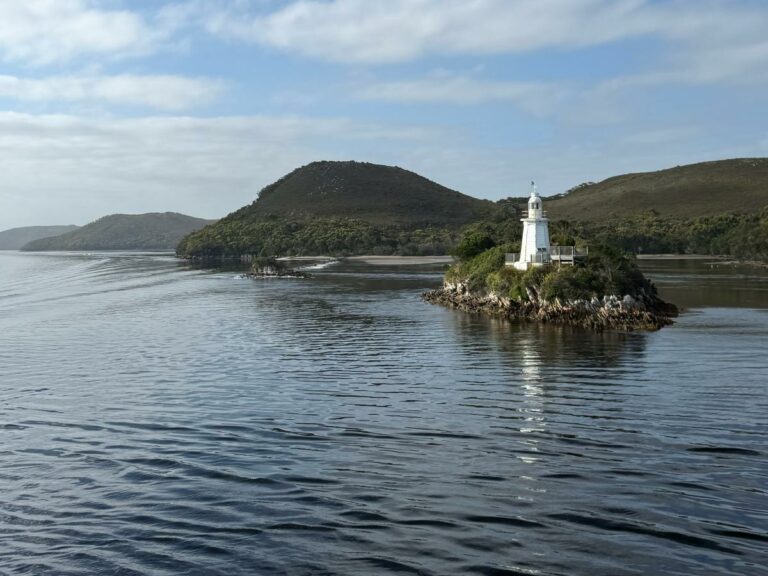 White lighthouse on rocky island in Gordon River with forested hills and water, Tasmania