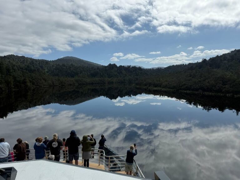 Group of tourists viewing mirror-like reflections on calm river surrounded by forested mountains in Tasmania