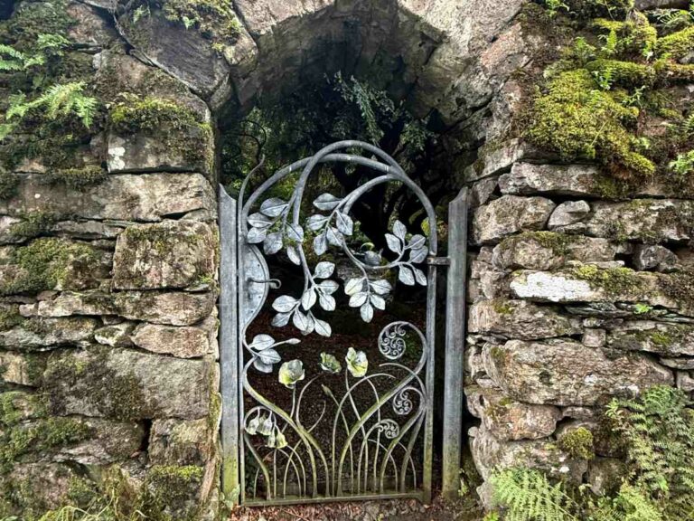 Ornate metal gate with leaf motifs set into moss-covered stone archway and walls