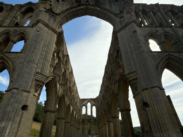 Ruins of Rievaulx Abbey with Gothic stone arches and columns reaching toward blue sky