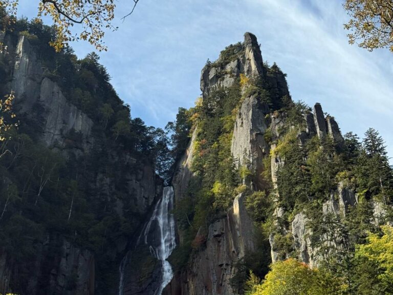 Tall limestone cliffs frame a waterfall cascading down a forested gorge valley