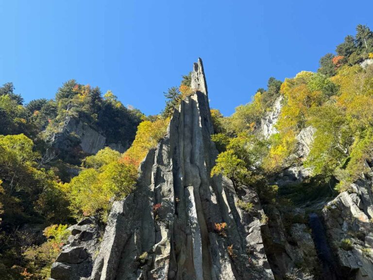 Tall rock spire rising through autumn forest foliage in Sounkyo Gorge hiking area