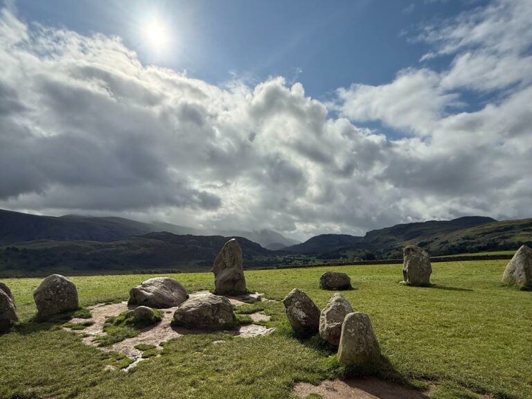 Ancient standing stones scattered across green valley floor with mountains and dramatic sky beyond