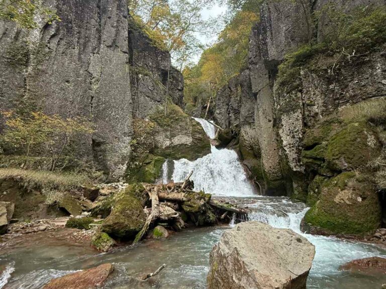 Waterfall cascading through moss-covered rocky gorge with stream and autumn foliage