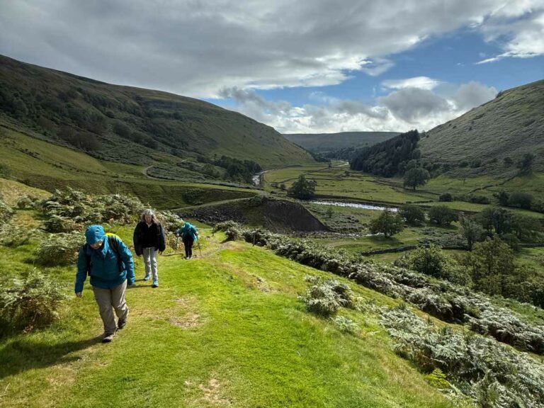 Group of walkers hiking through Yorkshire Dales rolling green hills with river valley